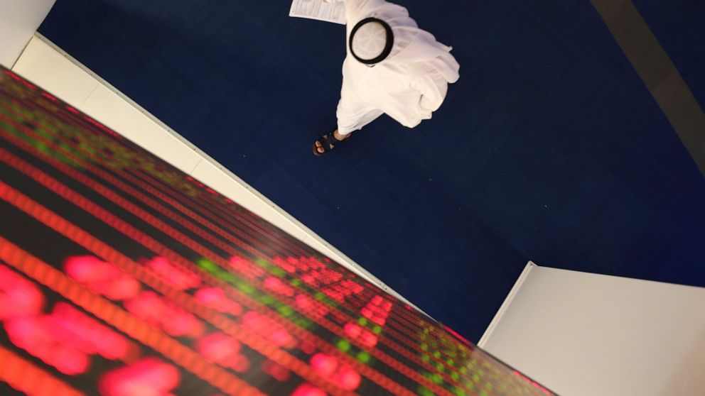 FILE - In this March 8, 2020, file, photo, an Emirati trader passes under the stocks display screen at the Dubai Financial Market in Dubai, United Arab Emirates. The United Arab Emirates will shut down its schools for four weeks as the coronavirus th