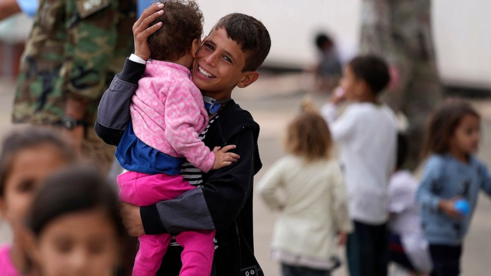 A recently evacuated young Afghan boy carries a child at the Ramstein U.S. Air Base, Germany, Tuesday, Aug. 24, 2021. The largest American military community overseas housed thousands of Afghan evacuees in an increasingly crowded tent city. (AP Photo