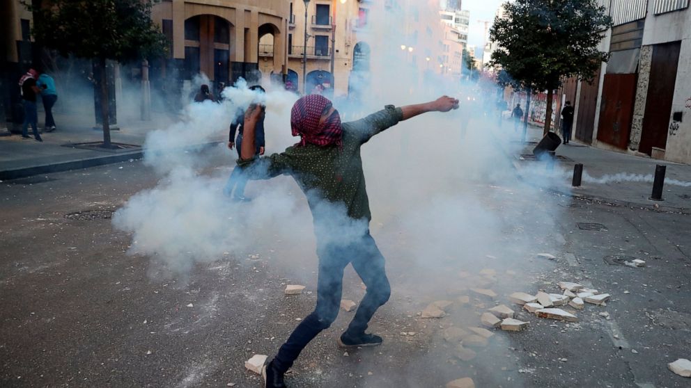 A protester throws back a tear gas canister towards riot policemen, during a protest near Parliament Square, In Beirut, Lebanon, Saturday, March. 13, 2021. Riot police fired tear gas to disperse scores of people who protested near parliament building