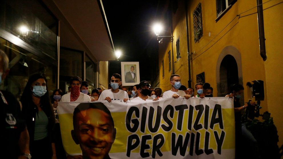 People walk holding a banner reading "Justice for WIlly" during a torch light procession in memory of Willy Monteiro Duarte, in Paliano, Italy, Wednesday, Sept. 9, 2020. Hundreds of people have walked in a funeral procession honoring a young Black ma