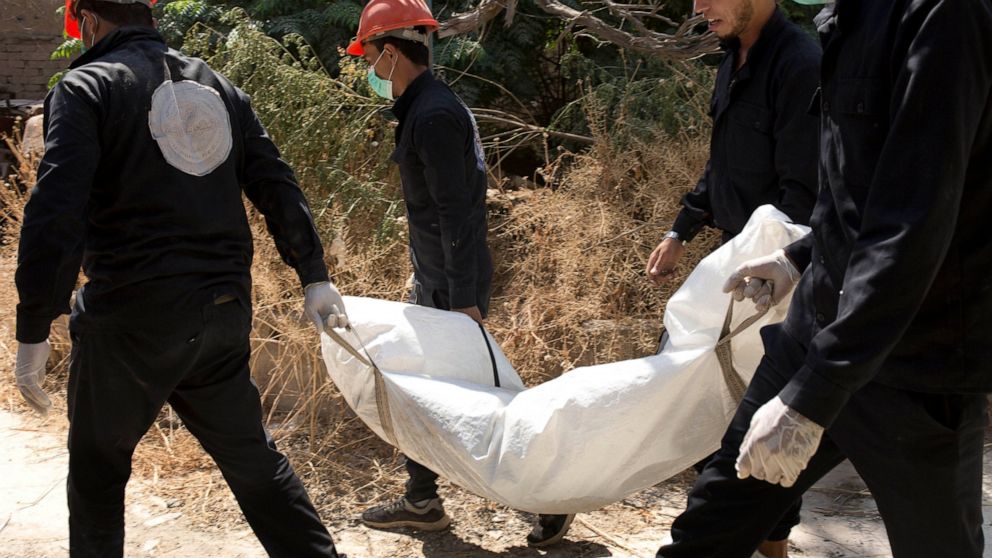 In this Saturday, Sept. 7, 2019, photo, first responders remove a body at the site of a mass grave in Raqqa, Syria. First responders say they have pulled nearly 20 bodies out of the latest mass grave uncovered in Raqqa, the Syrian city that was the d