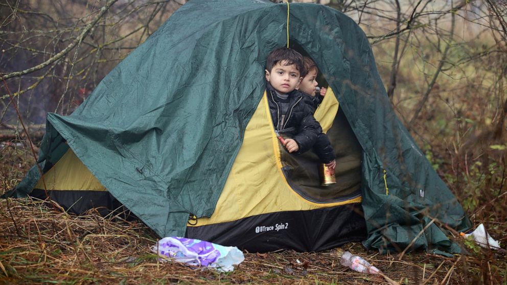Children look out from a tent as migrants gather at the Belarus-Poland border near Grodno, Belarus, Monday, Nov. 8, 2021. Poland increased security at its border with Belarus, on the European Union's eastern border, after a large group of migrants in