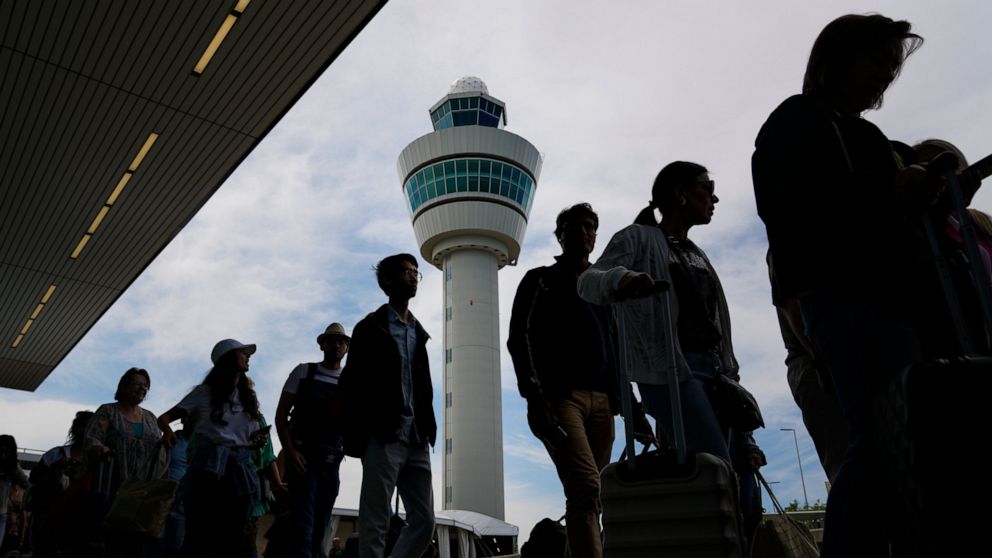 Travelers wait in long lines outside the terminal building to check in and board flights at Amsterdam's Schiphol Airport, Netherlands, Tuesday, June 21, 2022. The airport is reining in flight departures over its busy summer period because shortages o