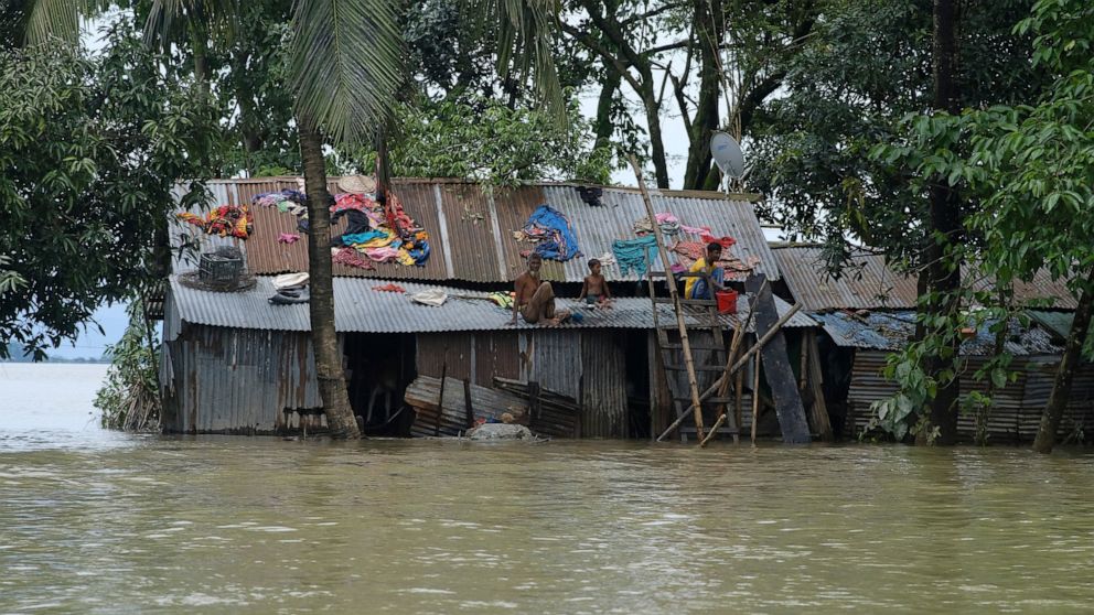 People sit on the tin roofs of their houses surrounded by flood waters in Sylhet, Bangladesh, Tuesday, June 21, 2022. Villagers in northeastern Bangladesh are crowding makeshift refugee centers and scrambling to meet boats arriving with food and fres