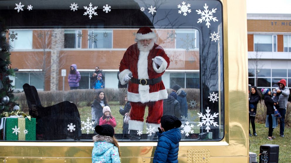 A man dressed as Santa Claus greets children from behind a glass enclosure in Vaughan, Ontario, Sunday, Dec. 13, 2020, after Vaughan Mills cancelled their seasonal in-person visits with Santa amid the continuing COVID-19 pandemic. York Region will go