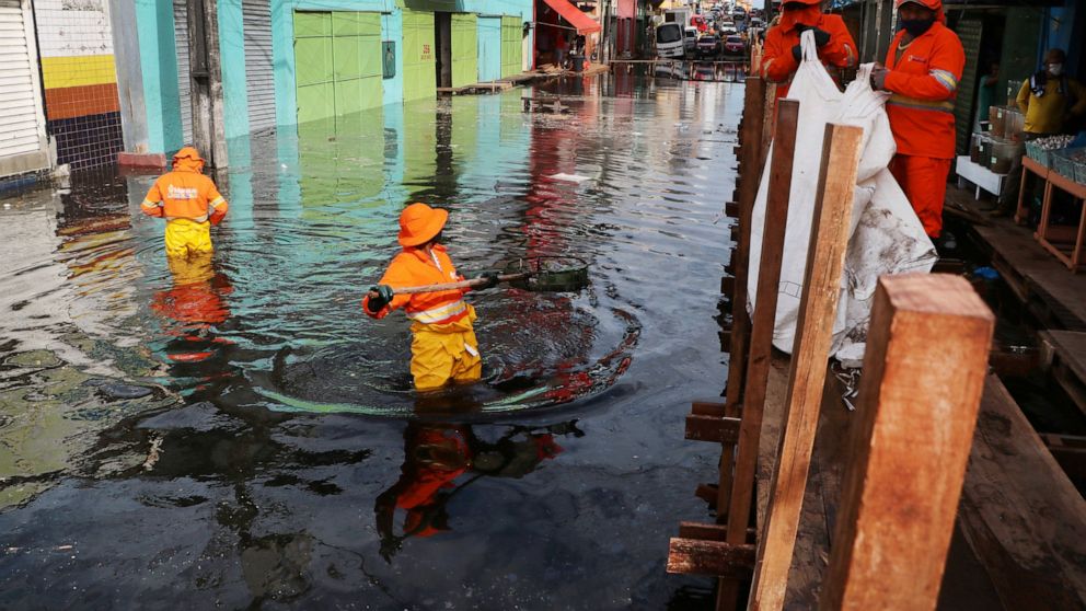 City workers pick trash from a street flooded by the waters of the Negro River in downtown Manaus, Brazil, Thursday, May 20, 2021. According to official records taken by the Port of Manaus, the city is facing one of its worse floods in years, with le