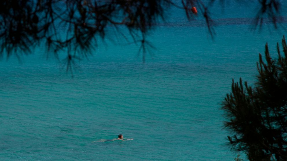 Sunday, May 10, 2020 photo, a lone swimmer wades through the clear waters of 'Konnos' beach in Ayia Napa, a seaside resort that's popular with tourists from Europe and beyond. Cyprus' beleaguered tourism sector got some good news after the government