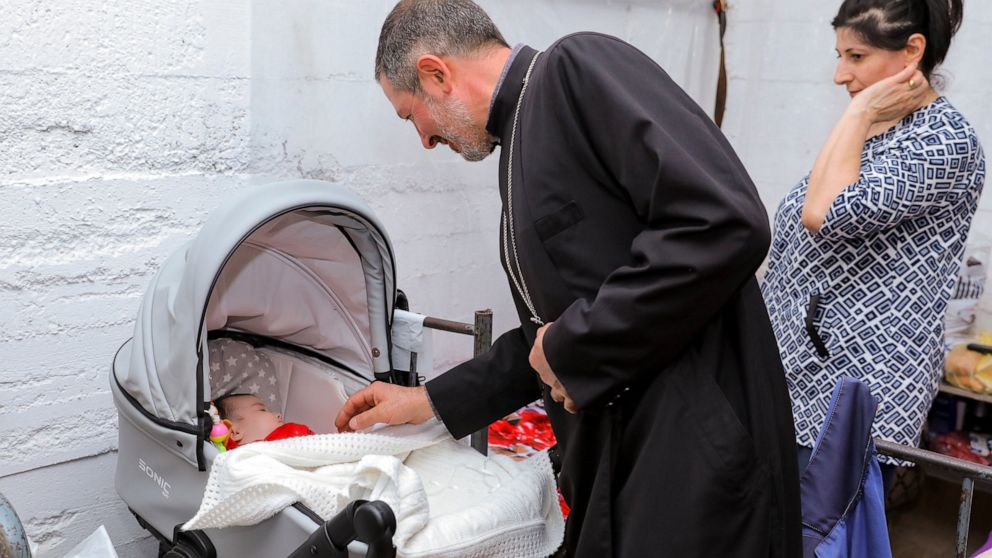 In this handout photo released by Armenian Foreign Ministry on Sunday, Sept. 27, 2020, an Armenian church priest looks a a baby in a bombshelter to protect against shelling in Stepanakert, the self-proclaimed Republic of Nagorno-Karabakh, Azerbaijan.