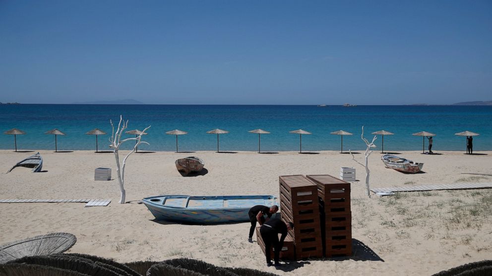 Workers arrange sunbeds as others install umbrellas at Plaka beach on the Aegean island of Naxos, Greece, Wednesday, May 12, 2021. With debts piling up, southern European countries are racing to reopen their tourism services despite delays in rolling