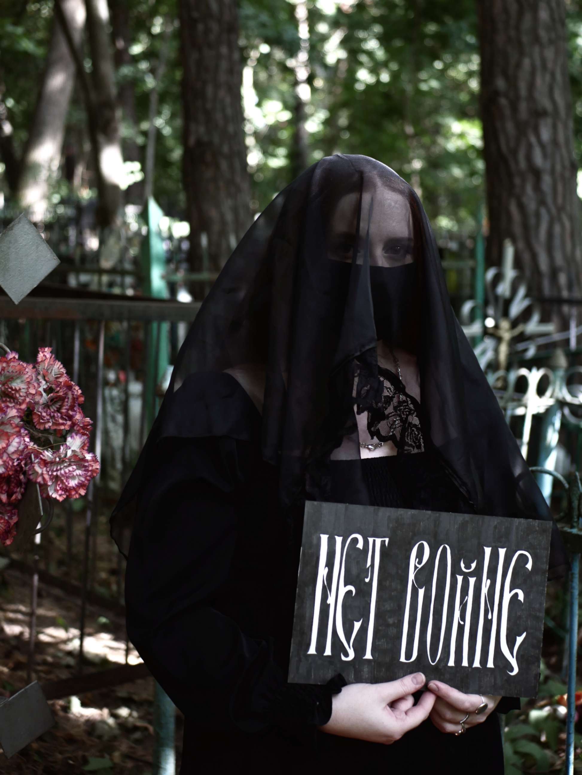 PHOTO: Anti-war activist, who asked to be called the pseudonym Elmatava, poses in traditional funeral attire with a sign that reads "no to war" in Cyrillic script, at a cemetery outside Moscow in late September.