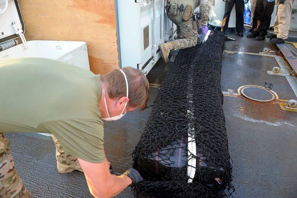 PHOTO: Two members of the United States Coast Guard cut the netting away from a large bale of cocaine on the deck of HMCS Whitehorse, part of the 1,500 kg of cocaine seized on April 5, 2018 during Operation CARIBBE. 