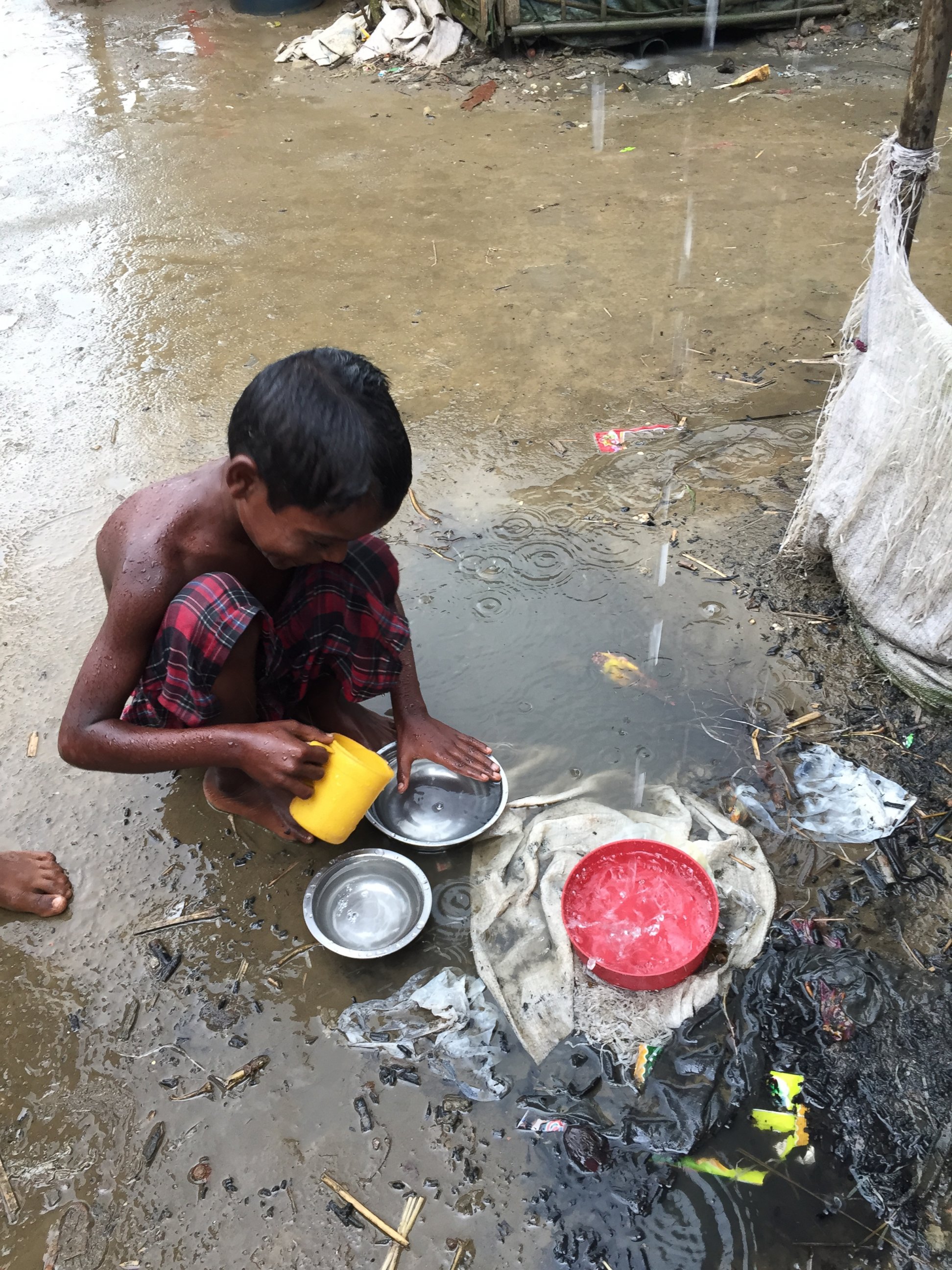 PHOTO: A young Rohingya boy in the refugee camp using rainwater to rinse dishes. 
