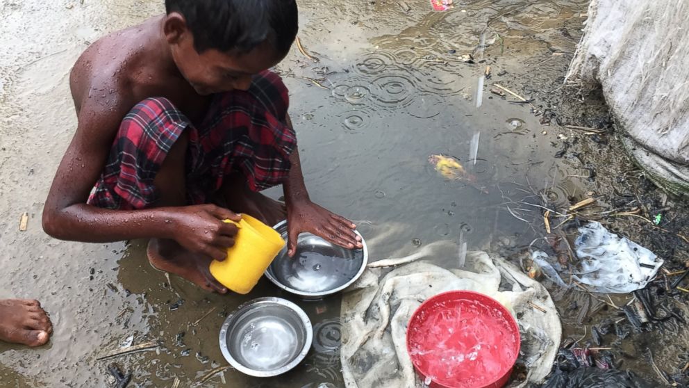 PHOTO: A young Rohingya boy in the refugee camp using rainwater to rinse dishes. 