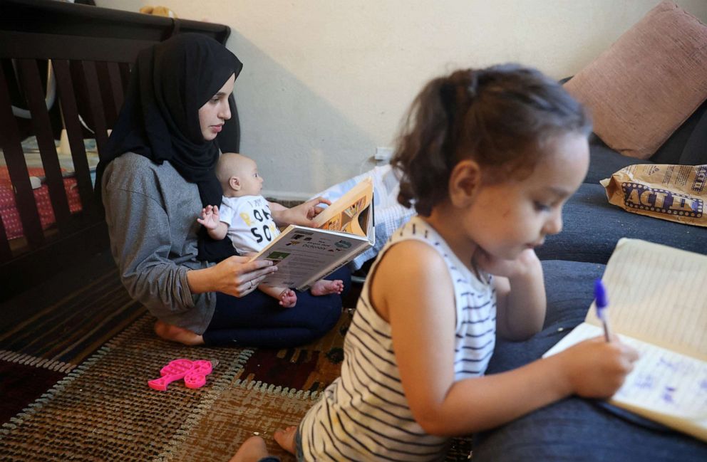 PHOTO: Susan Mohammadi looks over a Dari to English picture book to practice her English while she takes care of her two-month-old son, Yusuf Mohammadi, and daughter Zahra, 3, at their home in Sacramento, Calif., July 12, 2022.
