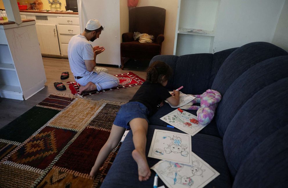 PHOTO: Zahra Mohammadi, 3, colors while her father Najib Mohammadi prays in the kitchen, at home in Sacramento, Calif., May 3, 2022.