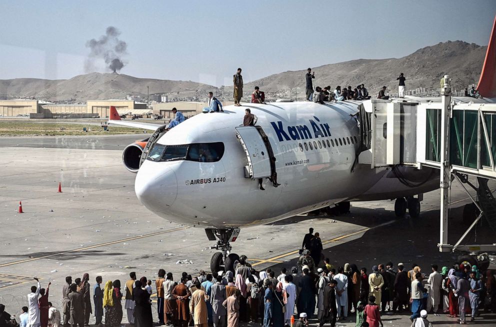 PHOTO: Afghan people climb atop a plane as they wait at the Kabul airport, Aug. 16, 2021, after a swift end to Afghanistan's 20-year war, as thousands of people mobbed the city's airport trying to flee the group's feared hardline brand of Islamist rule.