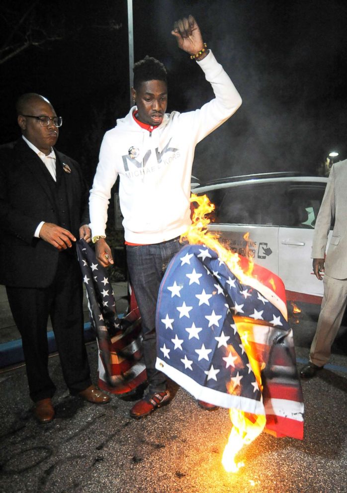 PHOTO: An activist drops a burning U.S. flag during a protest against the police shooting of a black man in an Alabama shopping mall in Hoover, Ala., Feb. 5, 2019.