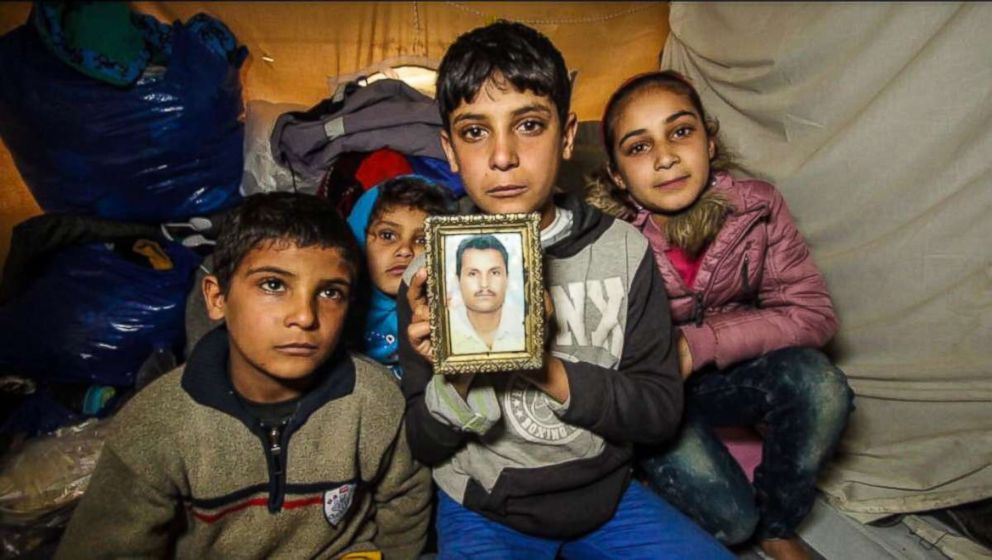 PHOTO: Anas Hommada, 14, sits in his tent in Lesbos' Moria camp with three of his siblings holding a photo of his missing father, Amer.