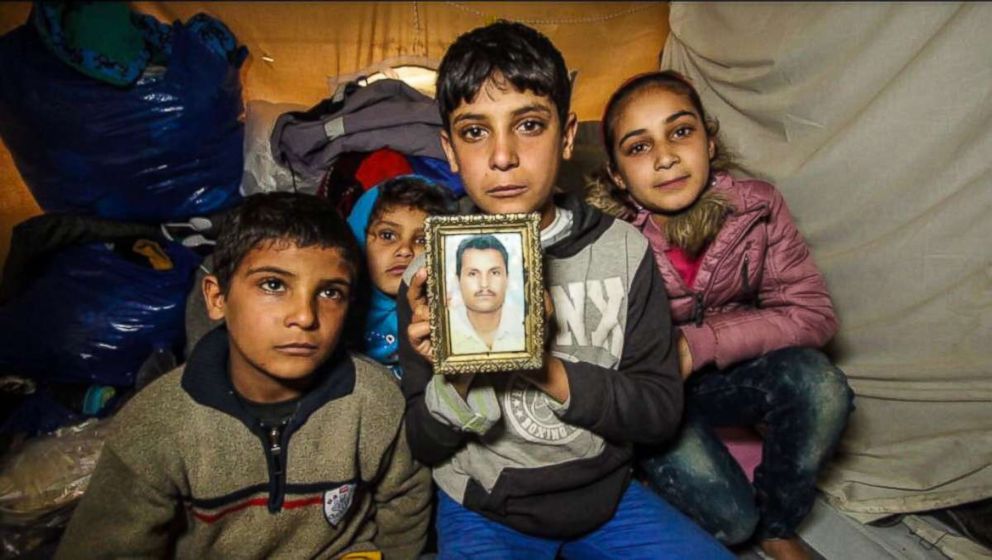  Anas Hommada, 14, sits in his tent in Lesbos Moria camp with three of his siblings holding a photo of his missing father, Amer.