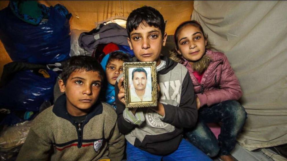 Anas Hommada, 14, sits in his tent in Lesbos' Moria camp with three of his siblings holding a photo of his missing father, Amer.