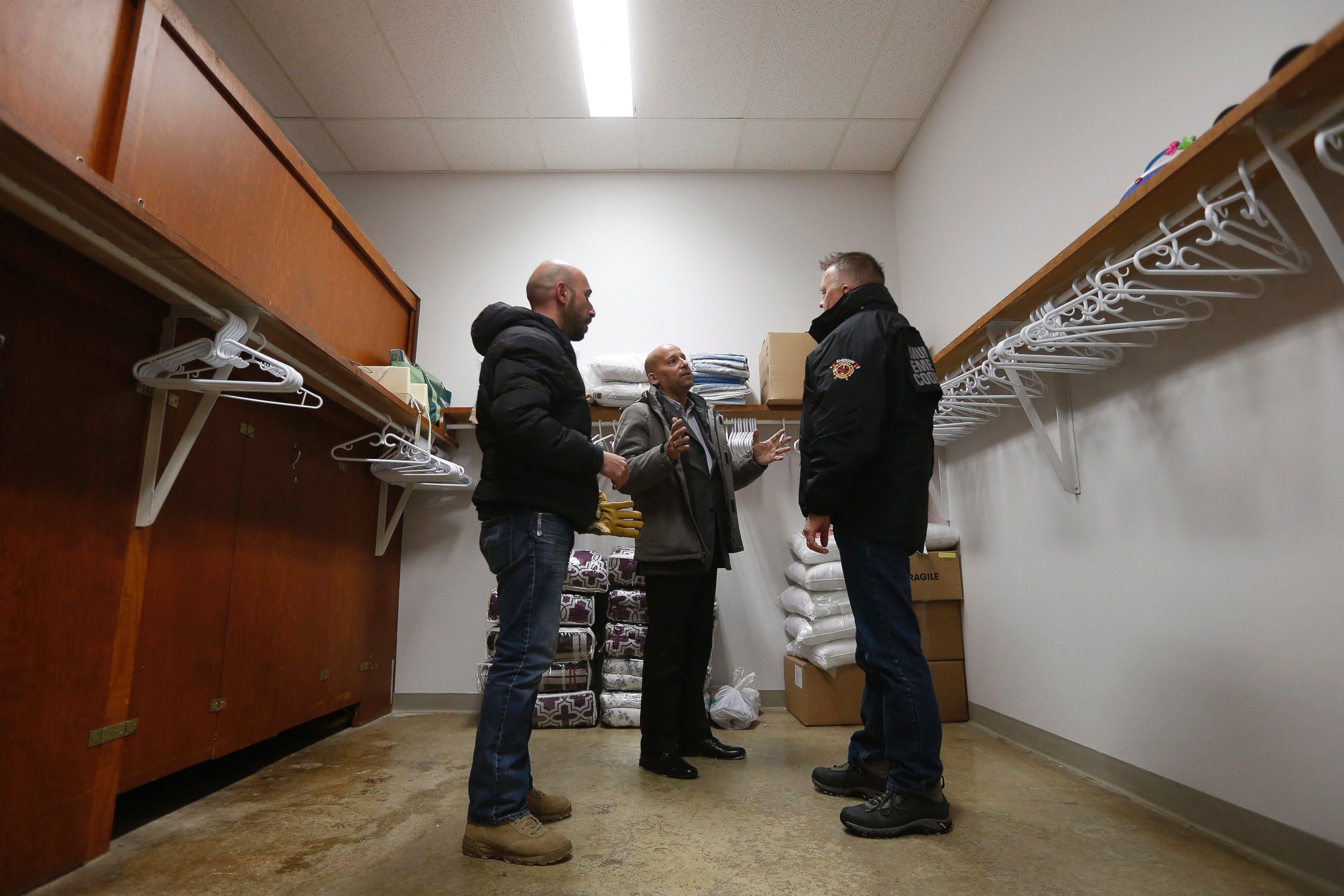 PHOTO: Fadel Alshawwa and Jean Pierre Venegas talk with Bill Spanjer, Municipal Emergency Coordinator for Emerson-Franklin, talk as they bring blankets and pillows into a community hall for refugees that may walk across the border in Emerson, Manitoba.