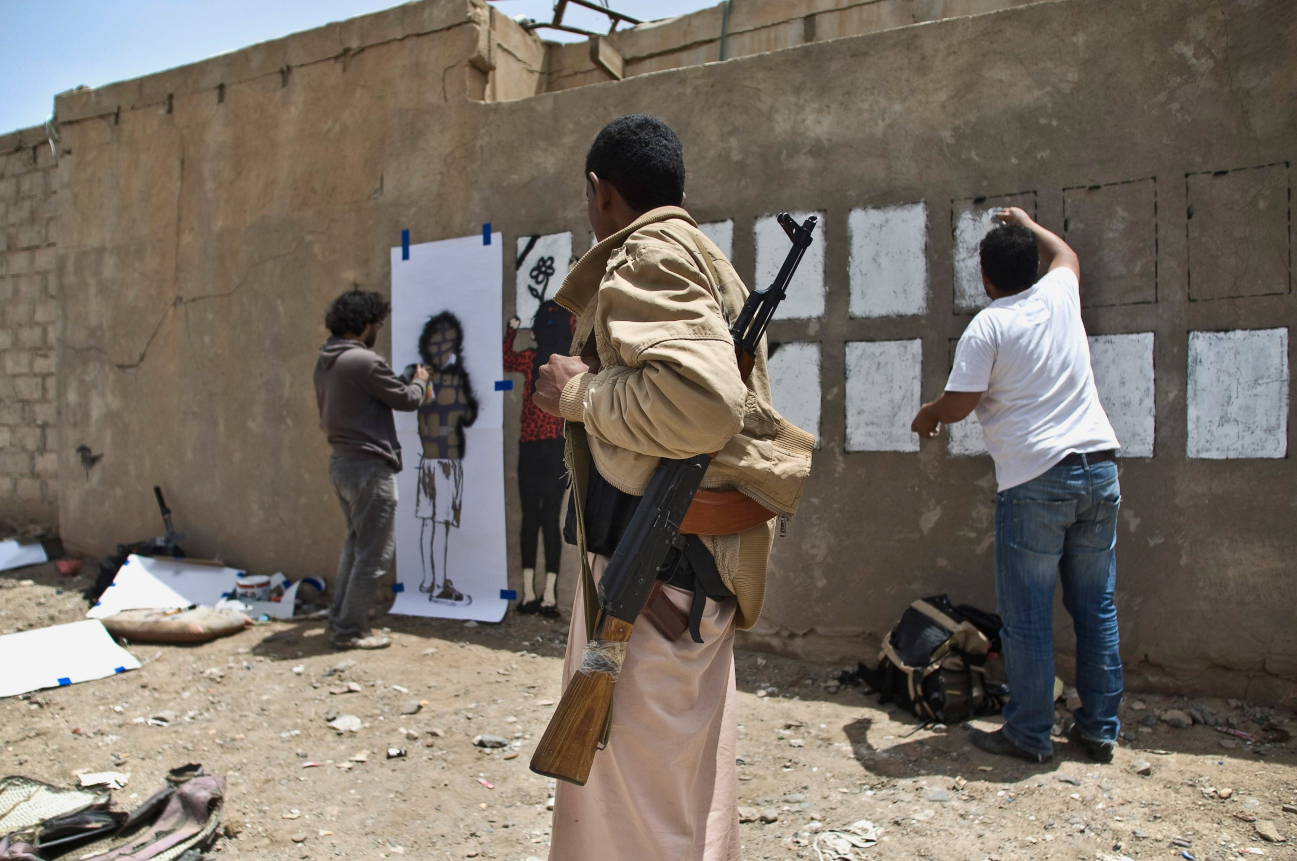 PHOTO: An armed man looks at Murad Subay and a collaborator spraying graffiti on a wall to commemorate the victims who were killed in Saudi-led coalition airstrikes in Sanaa, Yemen, May 18, 2015.