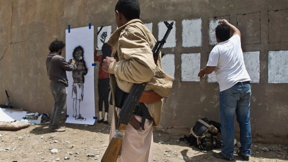 PHOTO: An armed man looks at Murad Subay and a collaborator spraying graffiti on a wall to commemorate the victims who were killed in Saudi-led coalition airstrikes in Sanaa, Yemen, May 18, 2015.