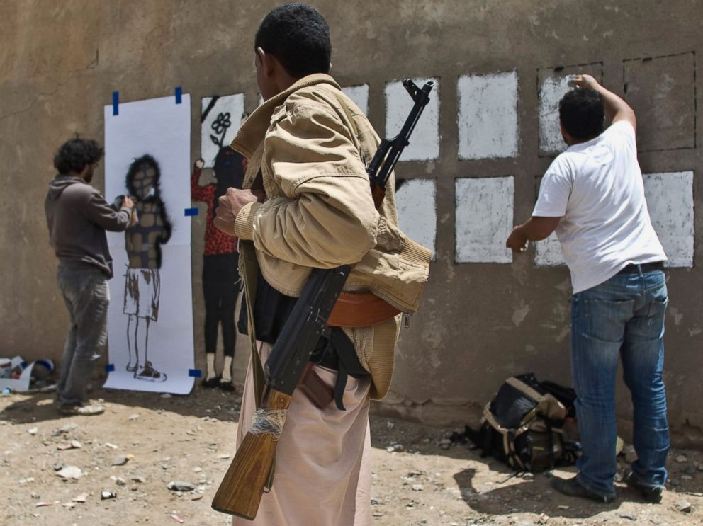 PHOTO: An armed man looks at Murad Subay and a collaborator spraying graffiti on a wall to commemorate the victims who were killed in Saudi-led coalition airstrikes in Sanaa, Yemen, May 18, 2015.