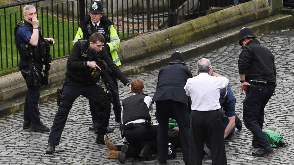 A policeman points a gun at a man on the ground as emergency services attend the scene outside the Palace of Westminster, London, March 22, 2017.