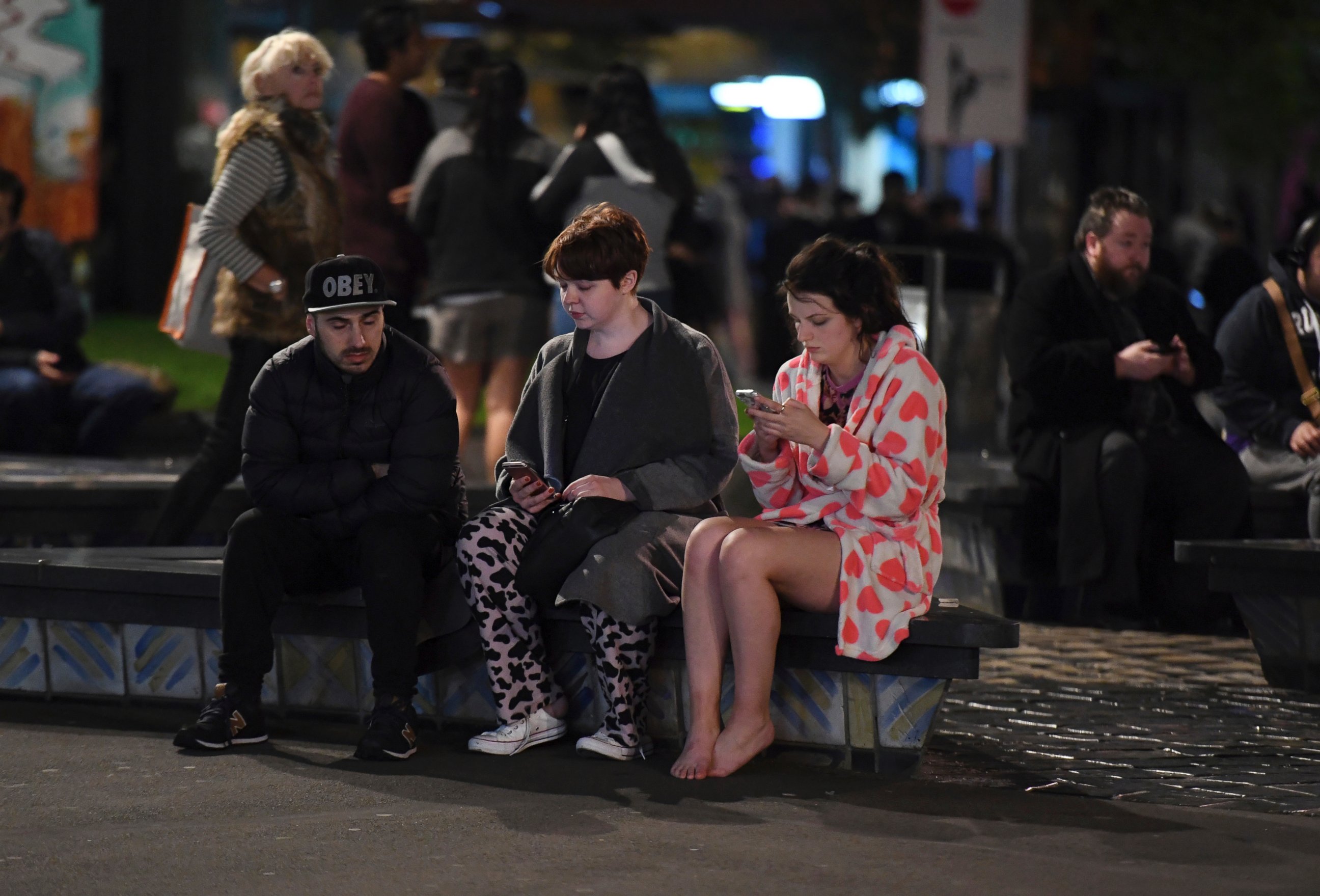 PHOTO: People evacuated from buildings along Dixon Street check their mobile phones while sitting on a bench in Wellington, New Zealand, after a 6.6 earthquake, Nov. 14, 2016.