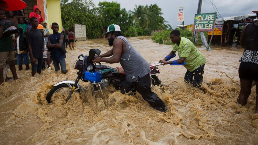 Two men push a motorbike through a street flooded by a nearby river that overflowed from heavy rains caused by Hurricane Matthew, in Leogane, Haiti, Oct. 5, 2016.