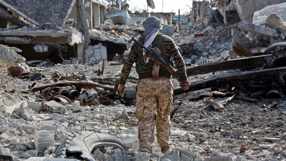 In this Nov. 19, 2014 file photo, a Kurdish People's Protection Units (YPG) fighter shows the extent of the damage from a truck bomb in Kobani, Syria. 