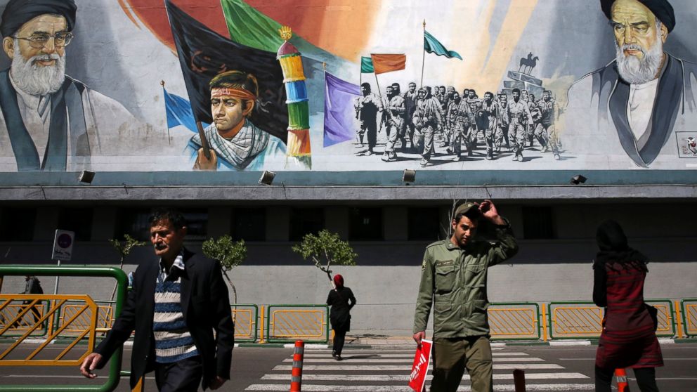Pedestrians cross the Enqelab-e-Eslami street under a mural depicting the late Iranian revolutionary founder Ayatollah Khomeini, right, members of Basij paramilitary force, center, and Supreme Leader Ayatollah Ali Khamenei, in Tehran, Iran, March 31, 2015.