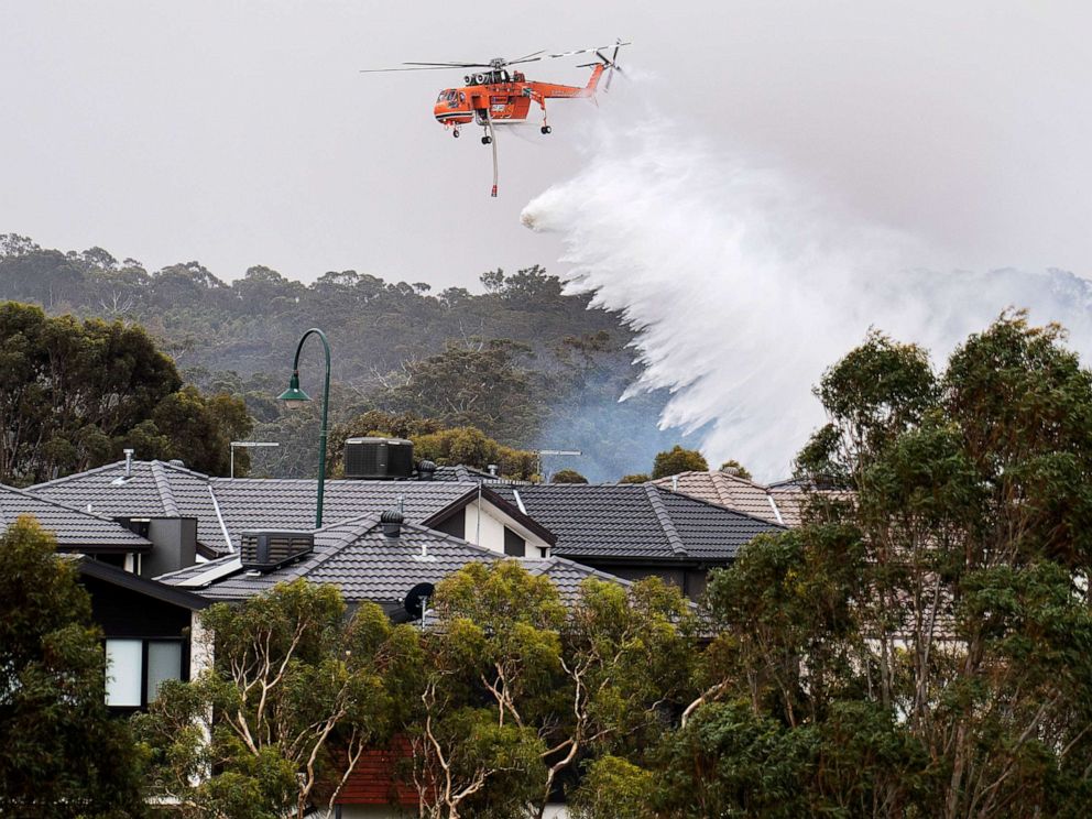 PHOTO: A skycrane drops water on a bushfire in scrub behind houses in Bundoora, Melbourne, Monday, Dec. 30, 2019.