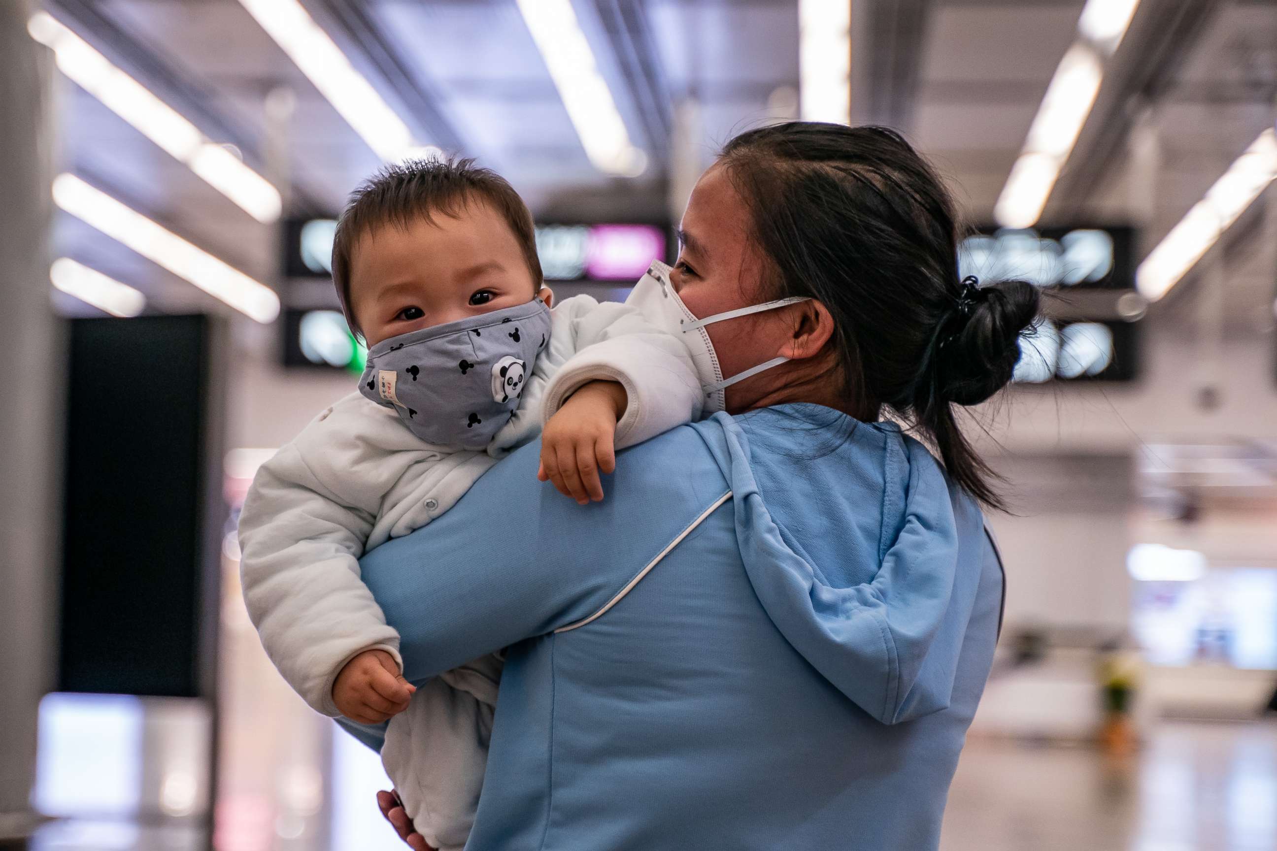 PHOTO: A woman carries a baby wearing a protective mask as they exit the arrival hall at Hong Kong High Speed Rail Station on Jan. 29, 2020.