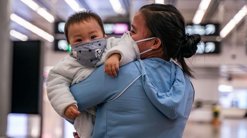 PHOTO: A woman carries a baby wearing a protective mask as they exit the arrival hall at Hong Kong High Speed Rail Station on Jan. 29, 2020.