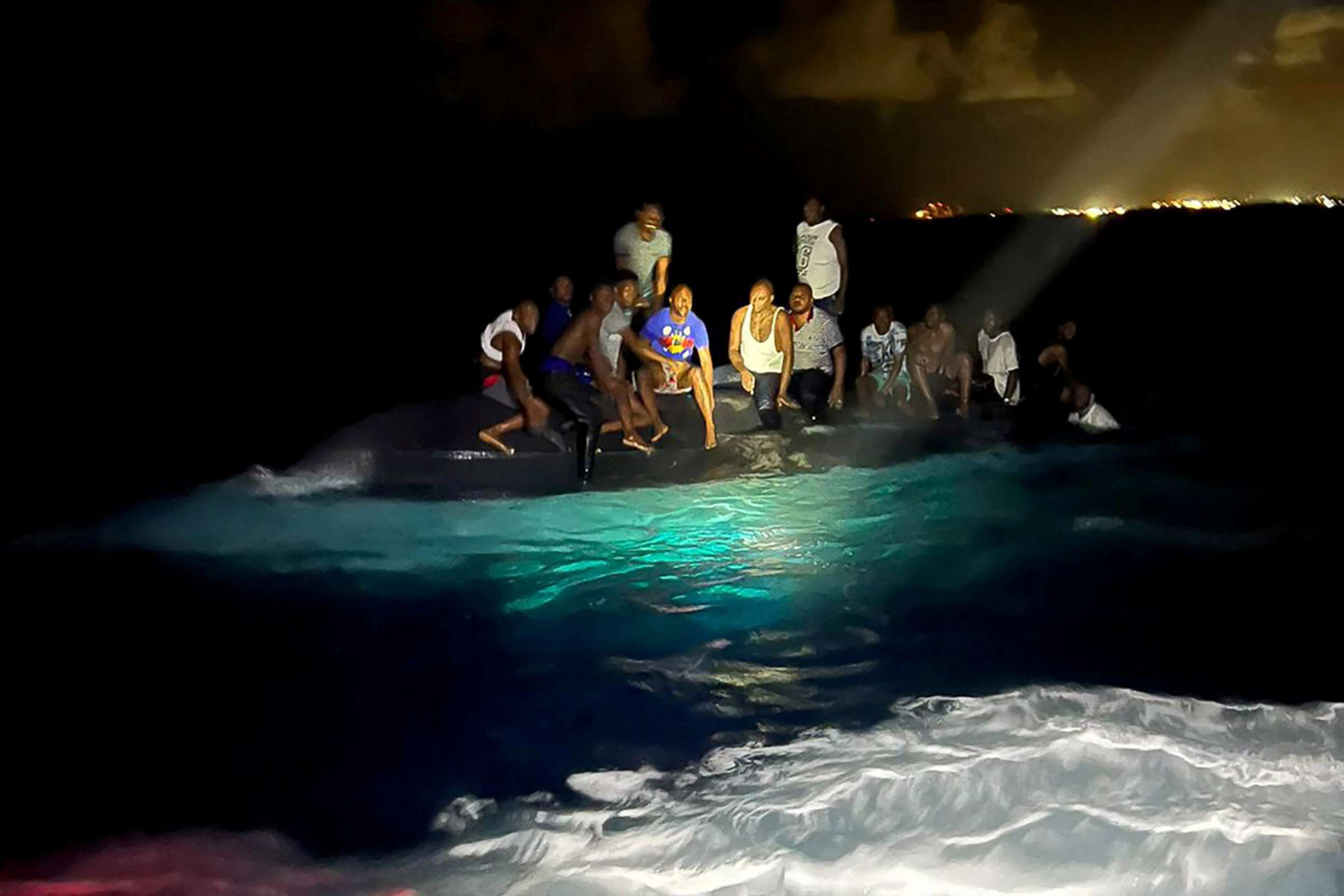 PHOTO: Survivors of a migrant boat that capsized perch on the overturned vessel off the coast of New Providence island, Bahamas, July 24, 2022. 