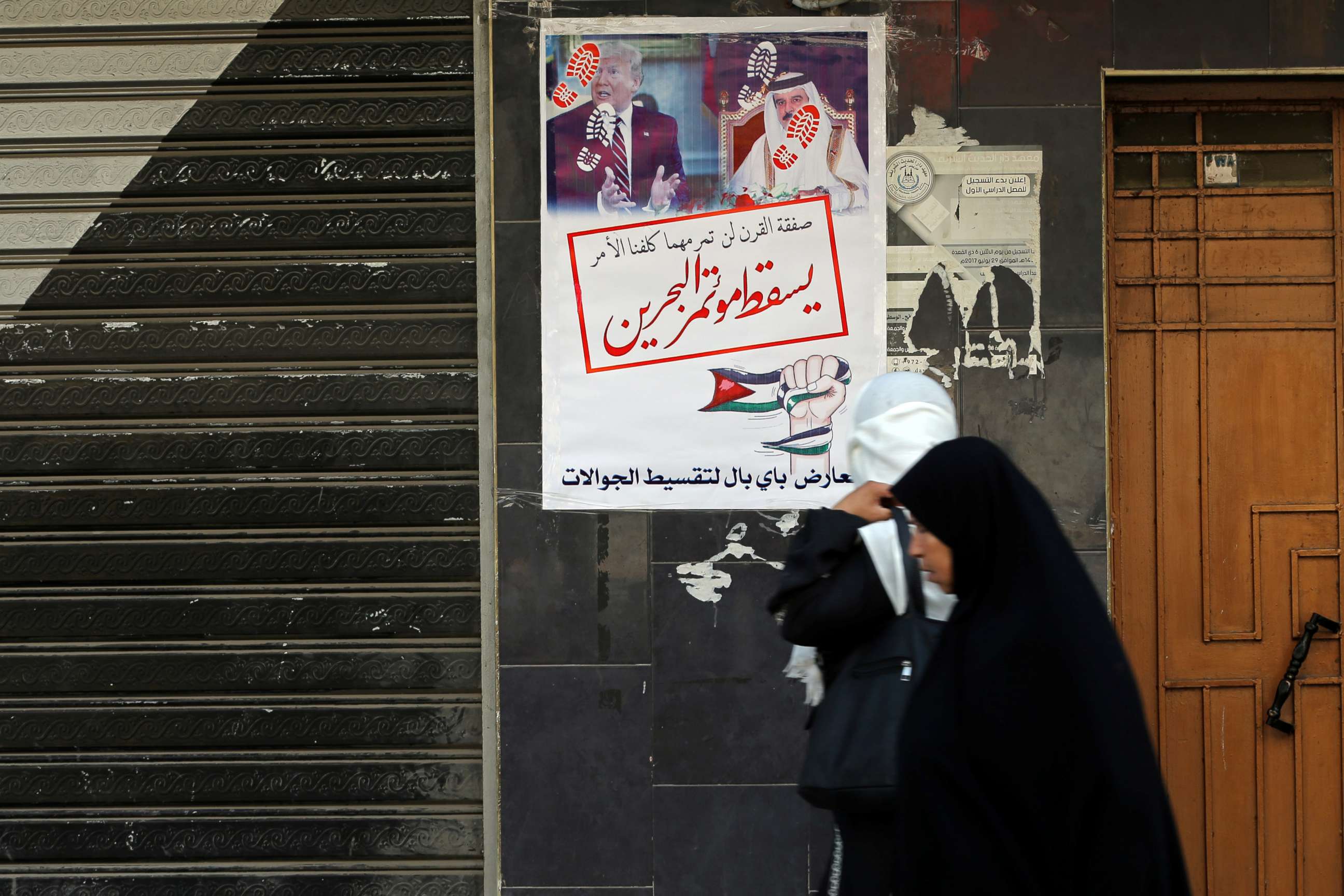 PHOTO: Women walk past banners showing pictures of Bahrain's King Hamad bin Isa Al Khalifa and U.S. President Donald Trump, reading "down with the Bahrain conference," in Khan Younis in the southern Gaza Strip, June 25, 2019.
