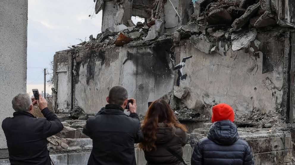 PHOTO: Local residents take photos of a work of world-renowned graffiti artist Banksy at the wall of destroyed building in the Ukrainian town of Borodianka, on Nov. 12, 2022.