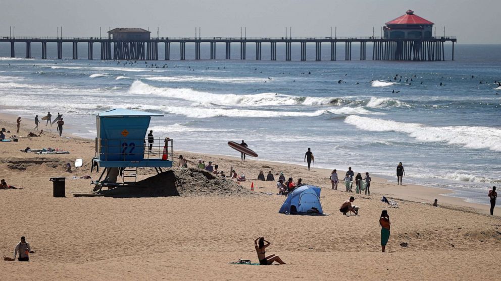 PHOTO: Beachgoers and surfers are seen at Huntington Beach, on April 22, 2020 in California. Southern California is expecting summer like weather over the next week as social distancing and beach closures continue due to the coronavirus (COVID-19). 