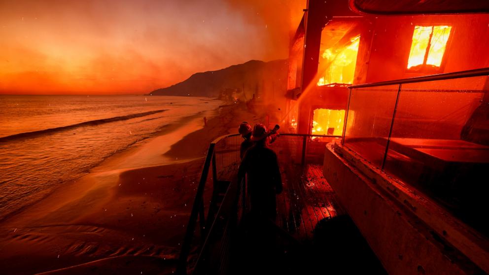 PHOTO: Firefighters work from a deck as the Palisades Fire burns a beachfront property, on Jan. 8, 2025, in Malibu, Calif.