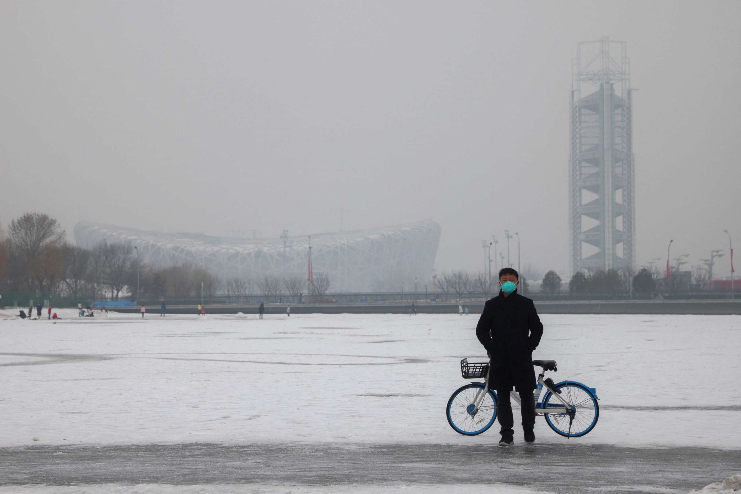 PHOTO: A man wearing a face mask stands on a frozen canal near the closed loop "bubble" surrounding venues of the Beijing 2022 Winter Olympics on a hazy day in Beijing, China, Jan. 24, 2022.