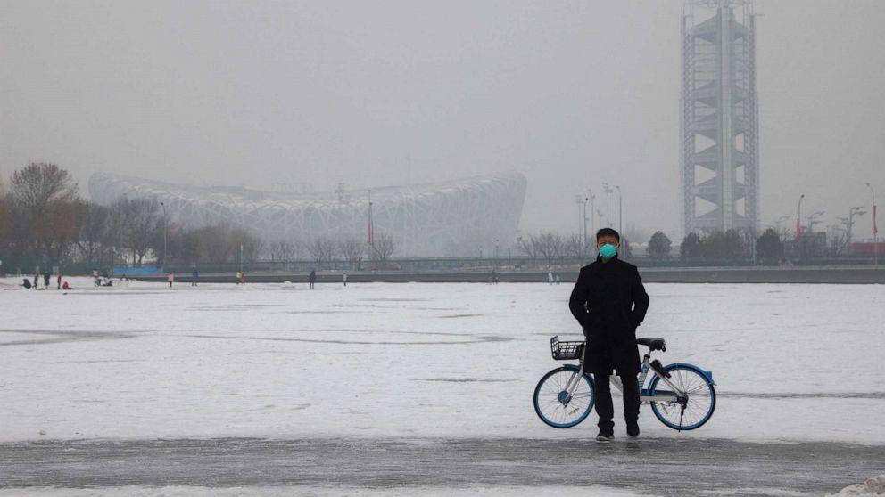 PHOTO: A man wearing a face mask stands on a frozen canal near the closed loop "bubble" surrounding venues of the Beijing 2022 Winter Olympics on a hazy day in Beijing, China, Jan. 24, 2022.