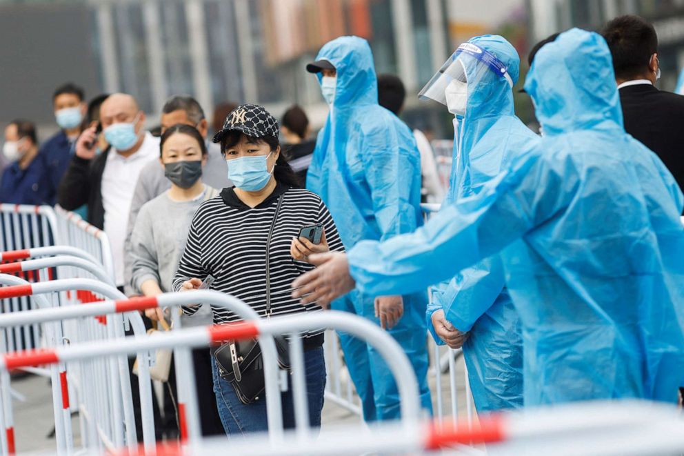 PHOTO: People wearing face masks walk next to medical workers wearing protective suits at a makeshift COVID-19 testing site in Beijing, China, April 25, 2022.