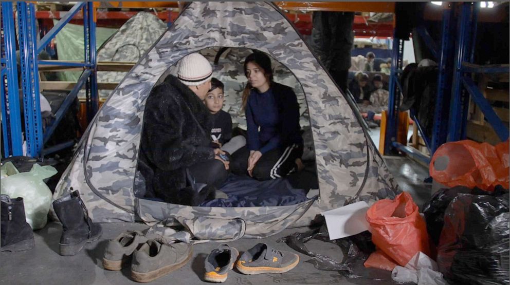 PHOTO: Karwan Jamal, an Iranian man with his wife Narin and their 7 year-old son, sitting in a tent under a shelf that is now there home in the warehouse.