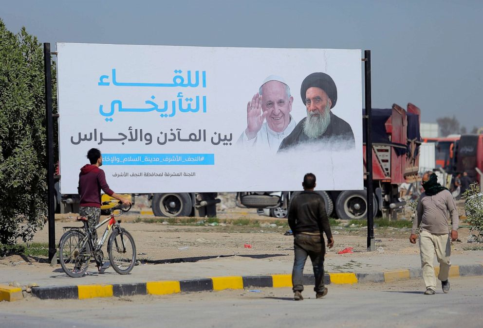 PHOTO: Iraqis walk by a poster announcing the upcoming visit of the Pope Francis and a meeting with a revered Shiite Muslim leader, Grand Ayatollah Ali al-Sistani, right, in Najaf, Iraq, March 3, 2021.