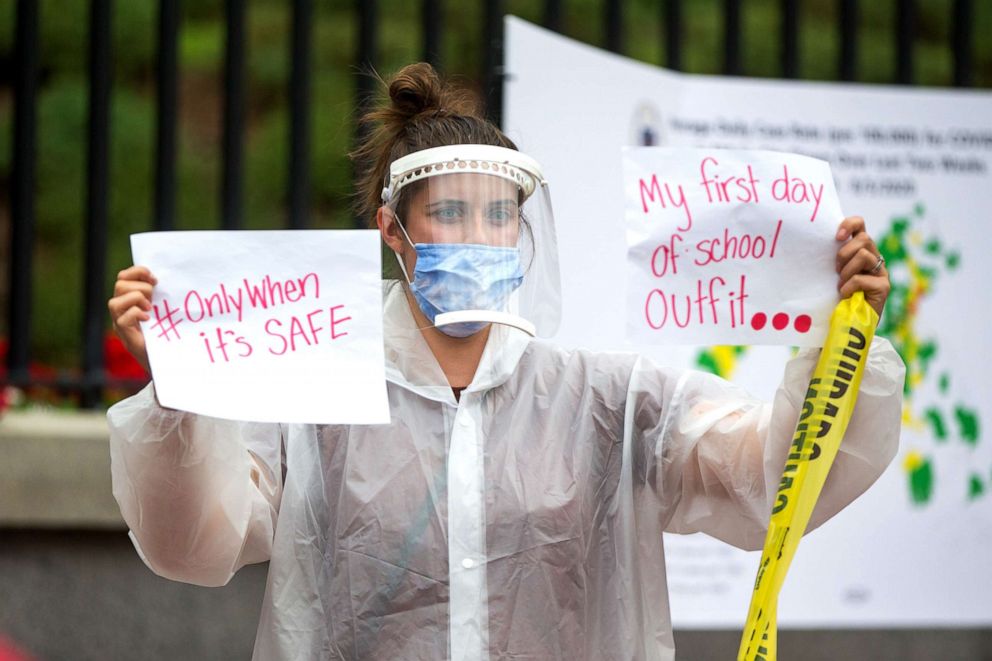 PHOTO: A woman in PPE holds up signs at a protest organized by the American Federation of Teachers at the Massachusetts State House on August 19, 2020, in Boston.