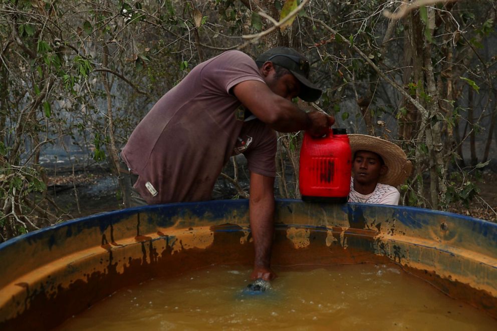 PHOTO: Carlos Augusto Rodrigues, 35, gives Rafael Silva, 16, a bottle filled with water to help put out a fire on a ranch in the Pantanal, the world's largest wetland, in Pocone, Mato Grosso state, Brazil, Aug. 28, 2020.