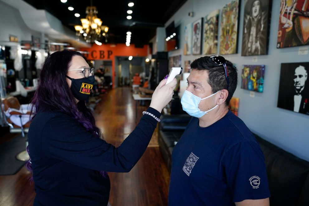 PHOTO: Melissa Acosta checks Rudy Pulido's temperature checked before a haircut at Orange County Barbers Parlor in Huntington Beach, Calif., in  July 15, 2020.