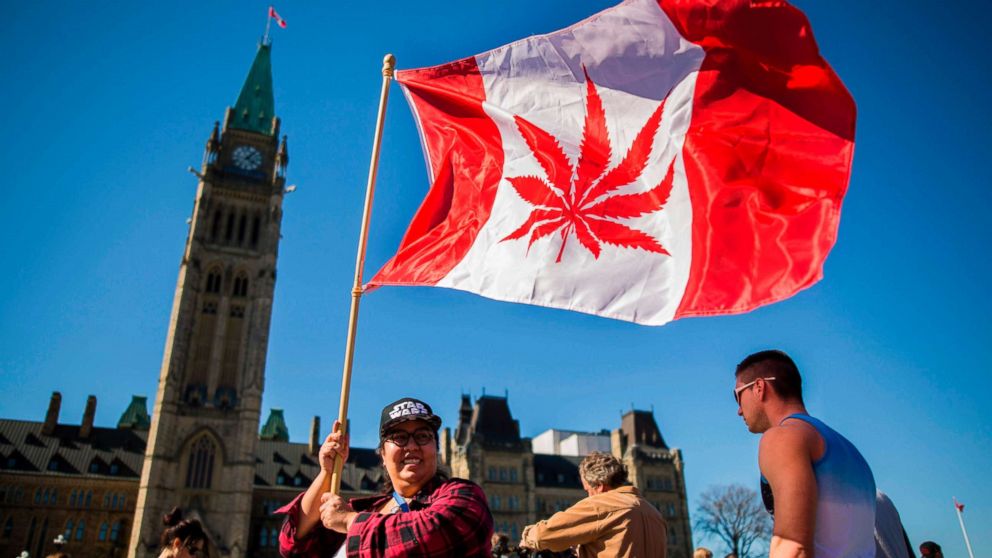 A woman waves a flag with a marijuana leaf on it next to a group gathered to celebrate National Marijuana Day on Parliament Hill in Ottawa, Canada.